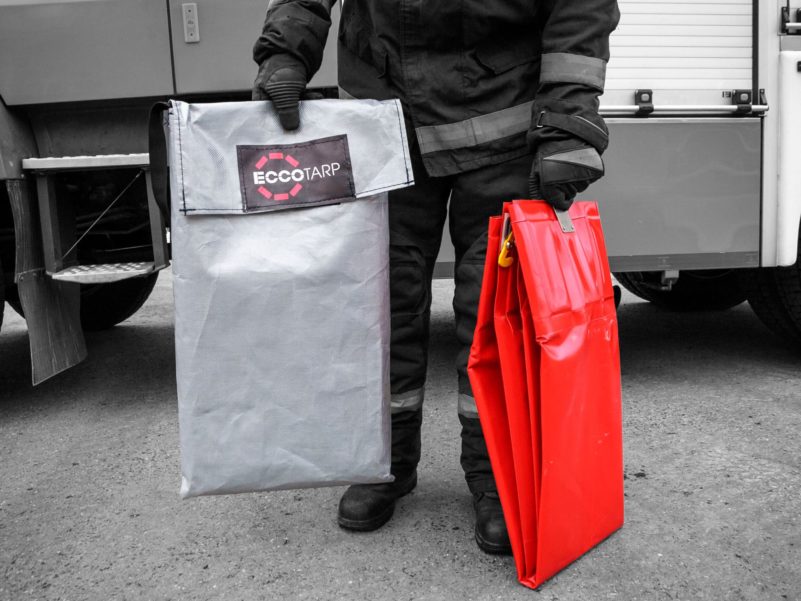 Firefighter holding Eccotarp and red equipment by truck.