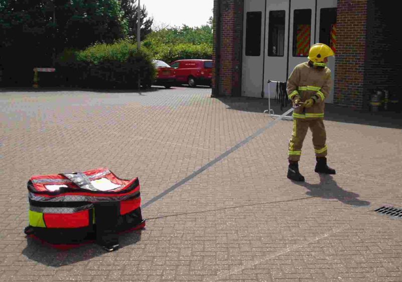 Firefighter pulling equipment in training yard.