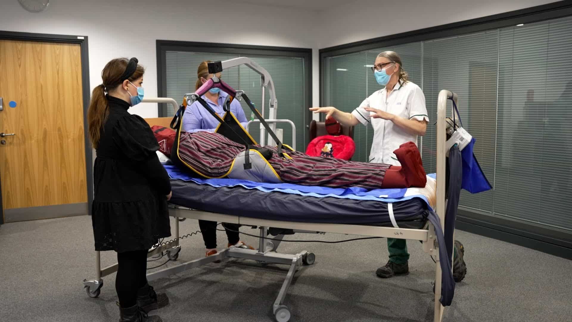 Nurses demonstrating patient hoist lift in care facility.