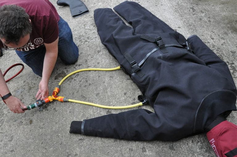 Person inflating a dry suit with a hose.