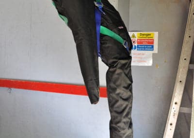 Suspended training dummy wearing safety harness indoors.