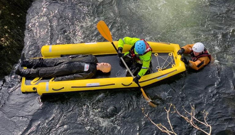 Rescue personnel navigating river with raft and individual.