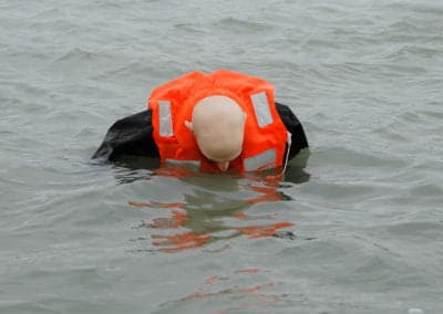 Person in life jacket floating face down in water.