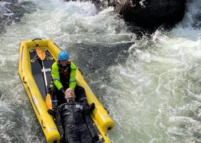 Rescue team navigating rapids with an unconscious person.