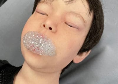 Child blowing a bubble on a grey background.