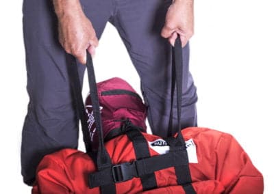 Person lifting red rescue dummy using straps.