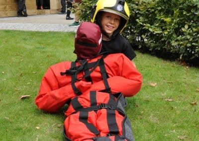 Child in firefighter gear practicing rescue, public event.