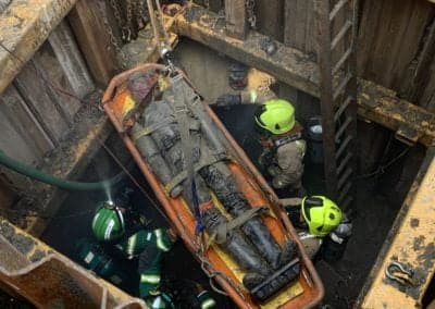 Firefighters rescuing worker from deep trench.