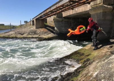 Rescue worker testing water rescue equipment under bridge.