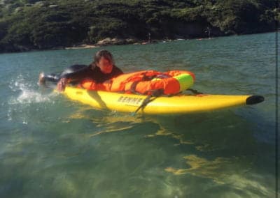 Person paddling a kayak with water rescue manikin and safety gear in water.
