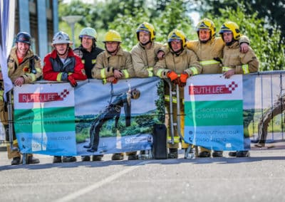 Firefighters posing in gear behind promotional banner.