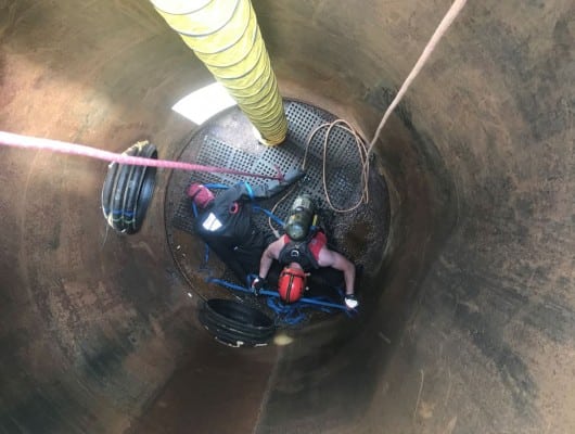 Worker in confined space with safety gear.