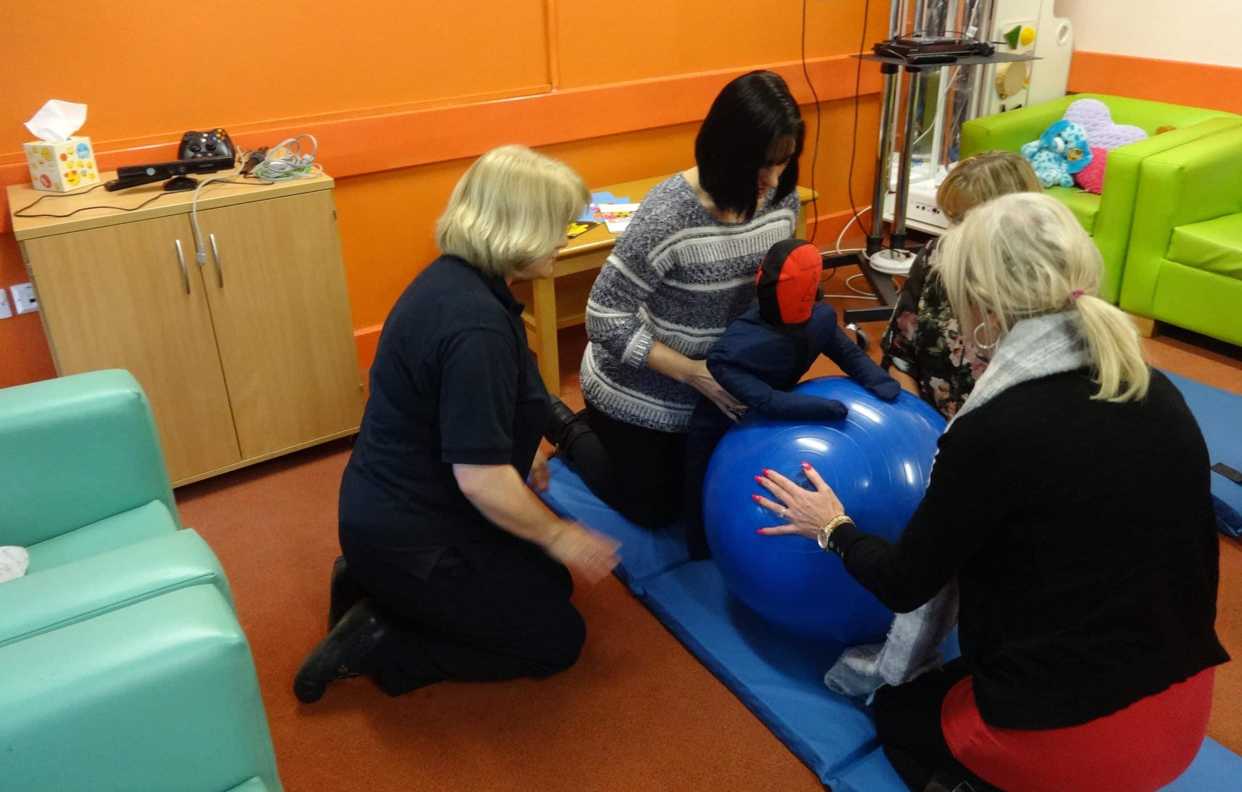 Therapists assisting child with developmental exercises using gym ball.