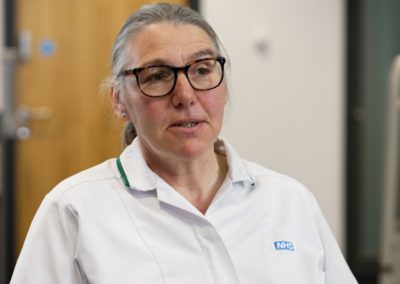 NHS nurse in uniform talking in a healthcare setting.