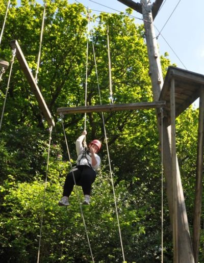 Person climbs high ropes course in forested area.